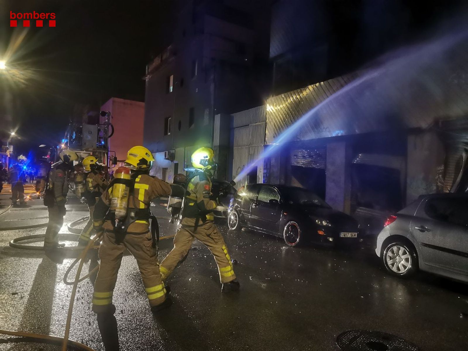 Dos bomberos echan agua a la fachada del edificio.