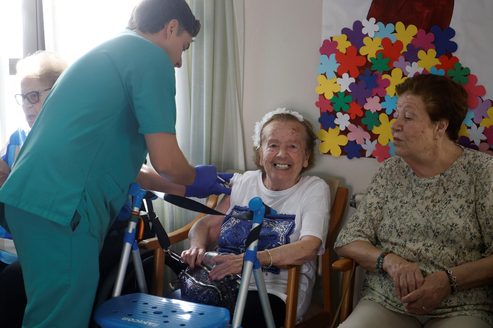 Una usuaria de una residencia de mayores sonríe mientras un enfermero le pone una vacuna.