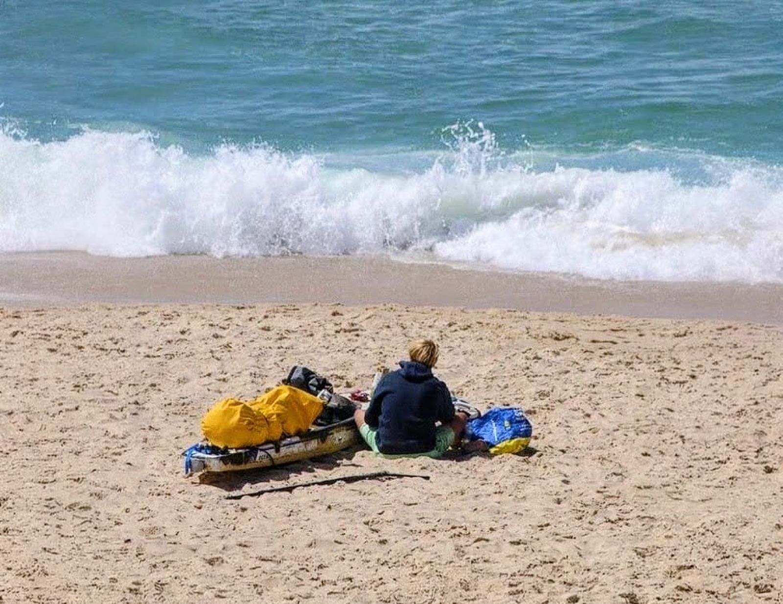 Sentado frente al mar en Balanegra, Jonas Böhlmark revisa su equipo junto a la tabla y la bolsa estanca con la que ha cruzado Europa, detenido por el viento antes de retomar la travesía.
