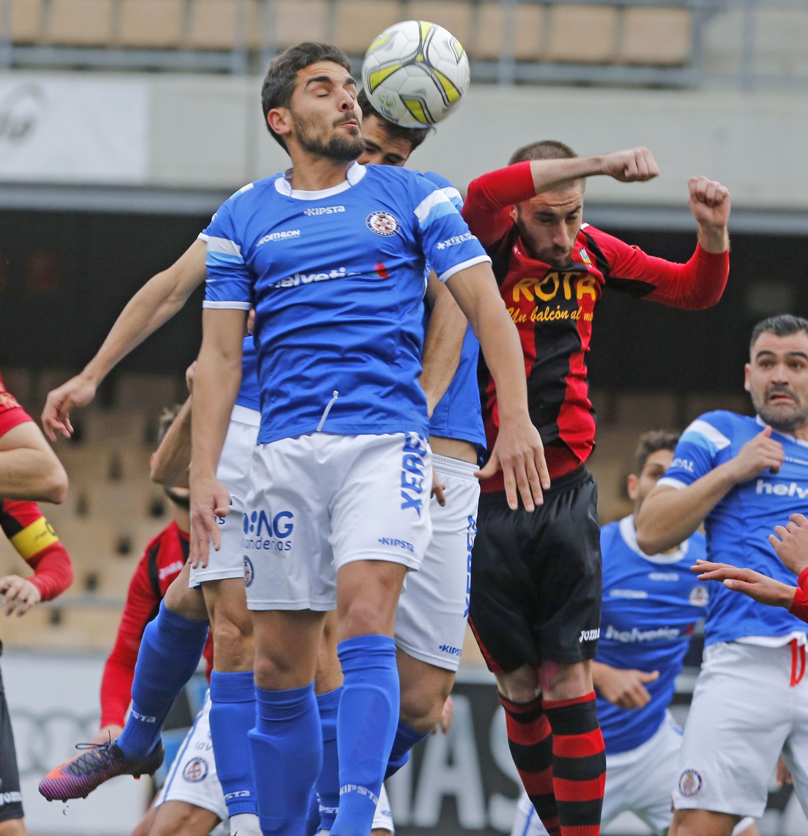 Joaqui, el último refuerzo de los azulinos, salta para despejar el balón de cabeza rodeado de jugadores rojillos.