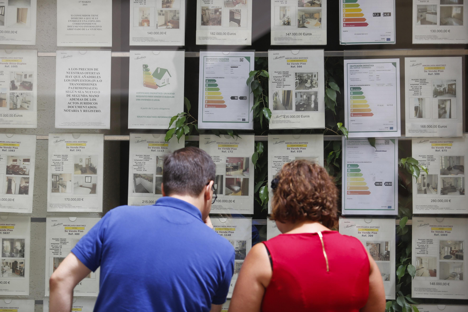 Dos personas miran el escaparate de una inmobiliaria en Málaga.