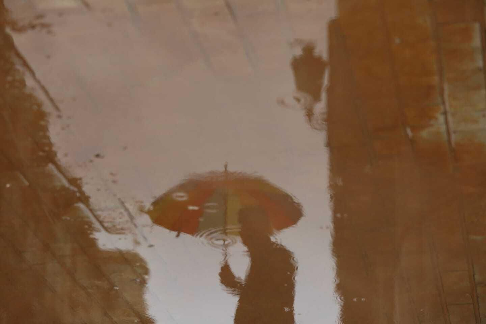 Reflejo de un transeúnte en los charcos de barro en Málaga.