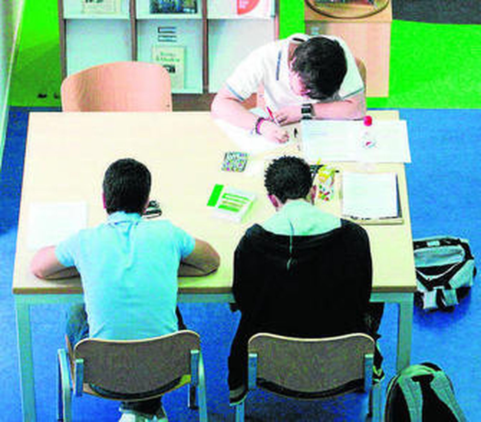 Tres alumnos estudian en una biblioteca.
