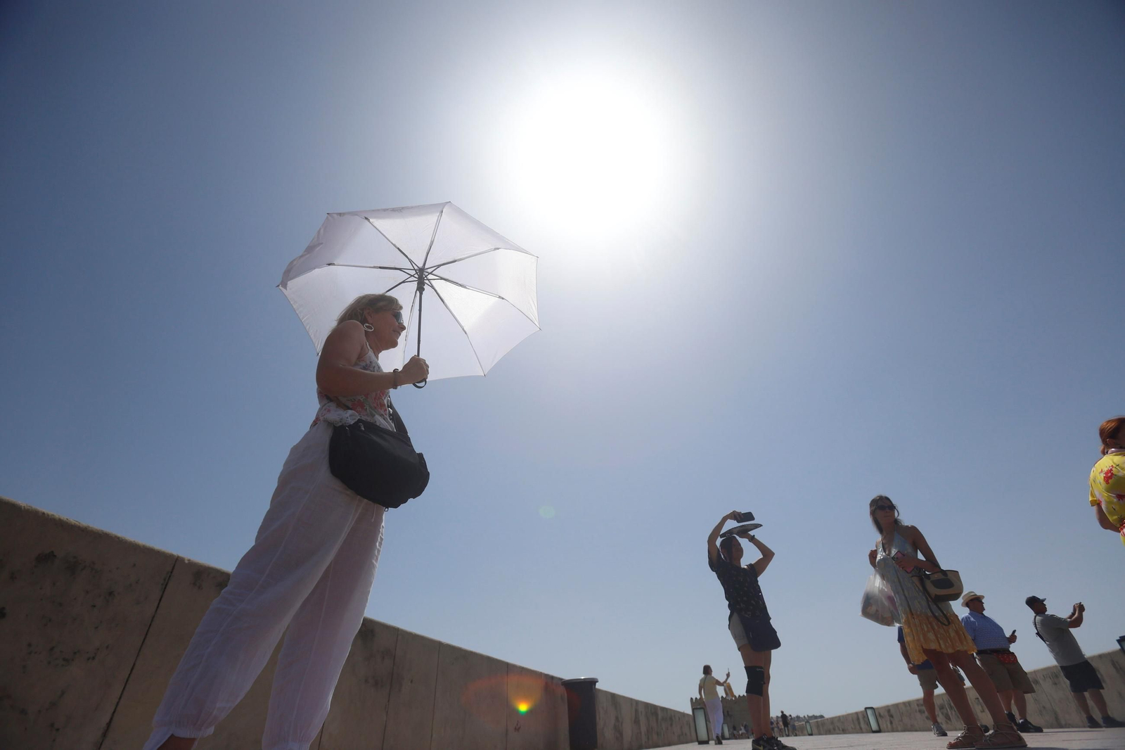 Una mujer se protege del sol con un paraguas en el Puente Romano.