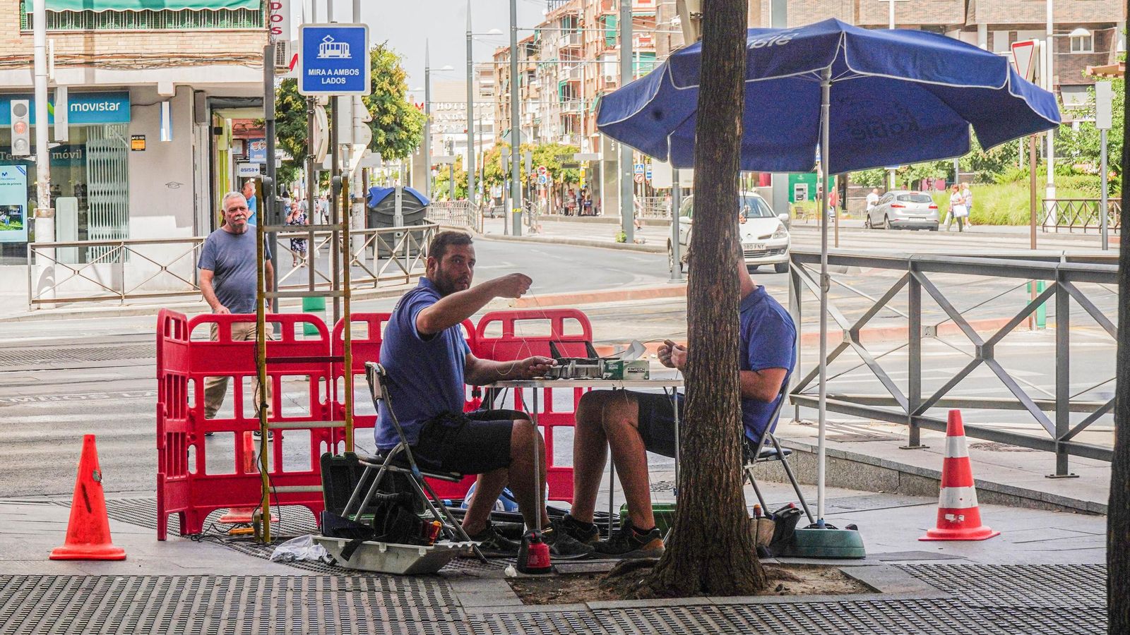 Obreros se protegen del sol con una sombrilla en plena calle en Granada Obreros se protegen del sol con una sombrilla en plena calle en Granada