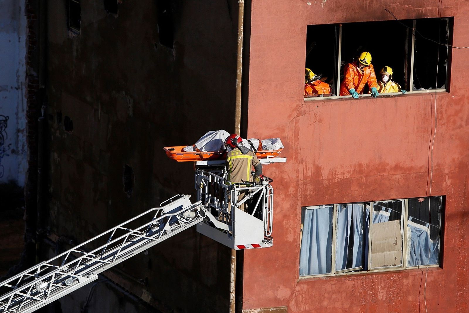 Los bomberos trasladan el cadáver de uno de los fallecidos de la nave incendiada la noche del miércoles en Badalona.