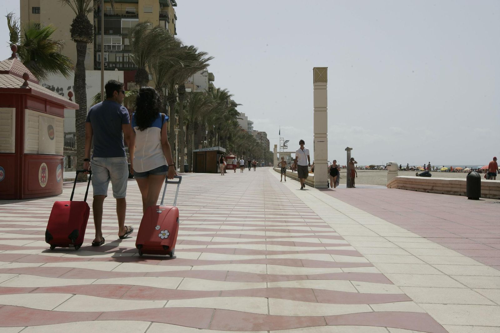 Una pareja con maletas recorre el paseo marítimo de Almería.