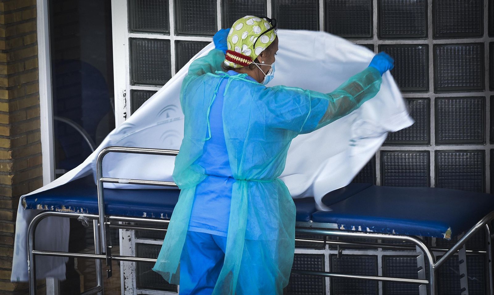 Un sanitario coloca una sábana limpia a una camilla.