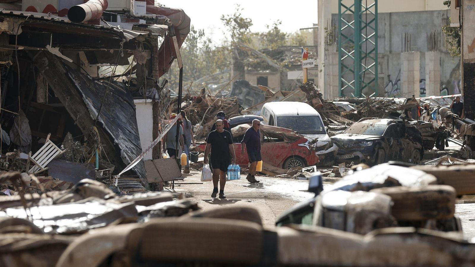 Varias personas caminan entre el lodo acumulado en las calles a causa de las intensas lluvias caídas por la fuerte dana