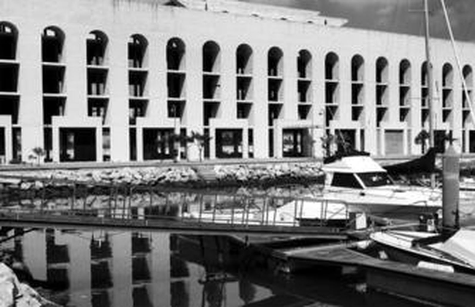 Uno de los pantalanes de Puerto Sherry con el segundo hotel, cuyas obras se paralizaron hace años, al fondo.