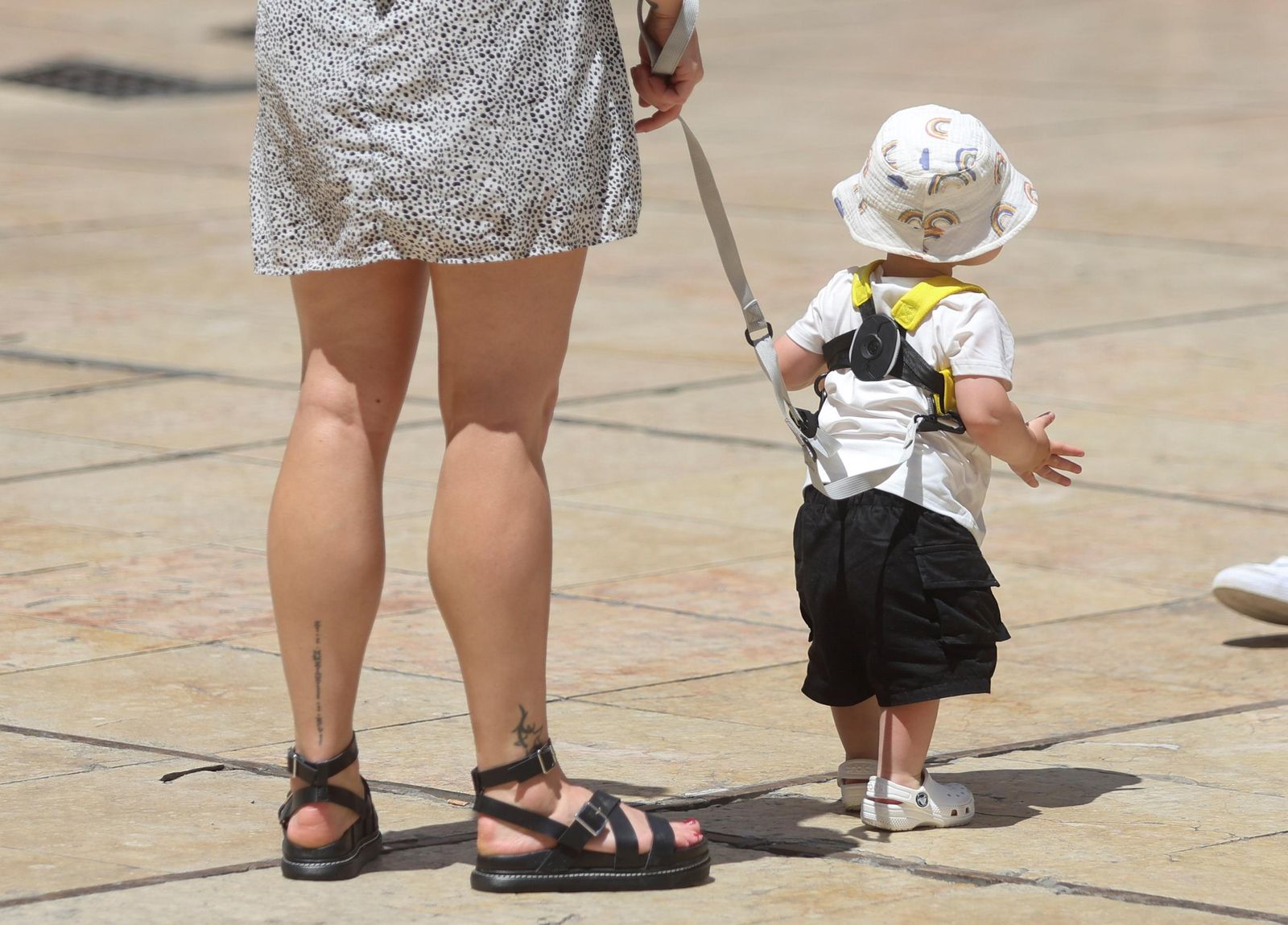 Una madre pasea nunto a su hijo, al que lleva cogido con un cordón.