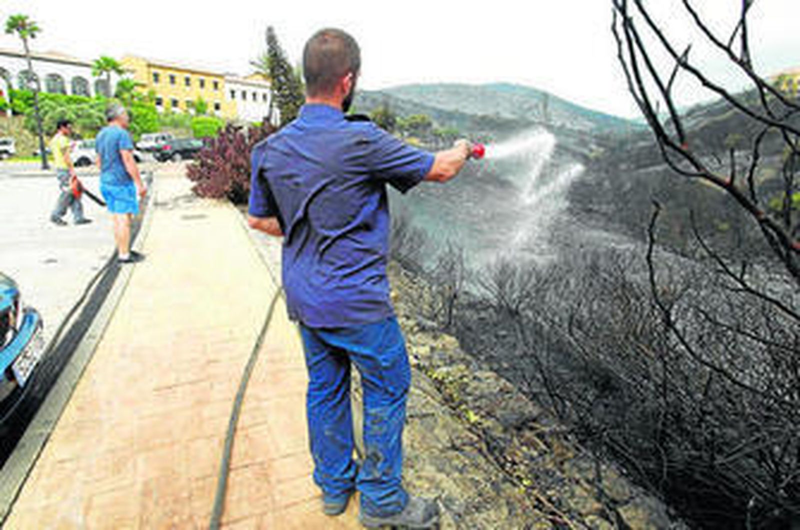 Un hombre refresca la zona que quedó calcinada junto a las viviendas de la Alcaidesa.