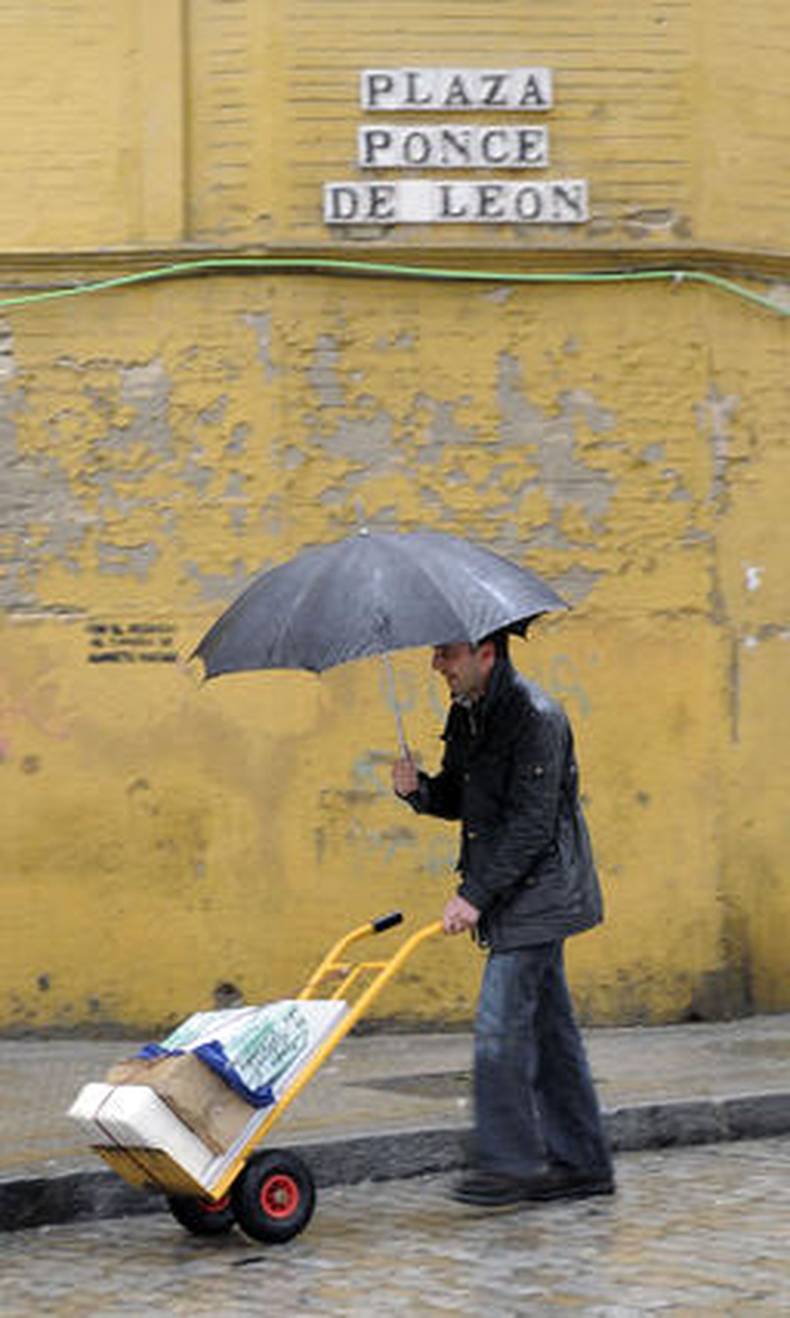 Un hombre empuja una carretilla con una mano mientras con la otra sujeta un paragüas para evitar mojarse.

Foto: J. C. Vázquez, B. Vargas y A. Pizarro