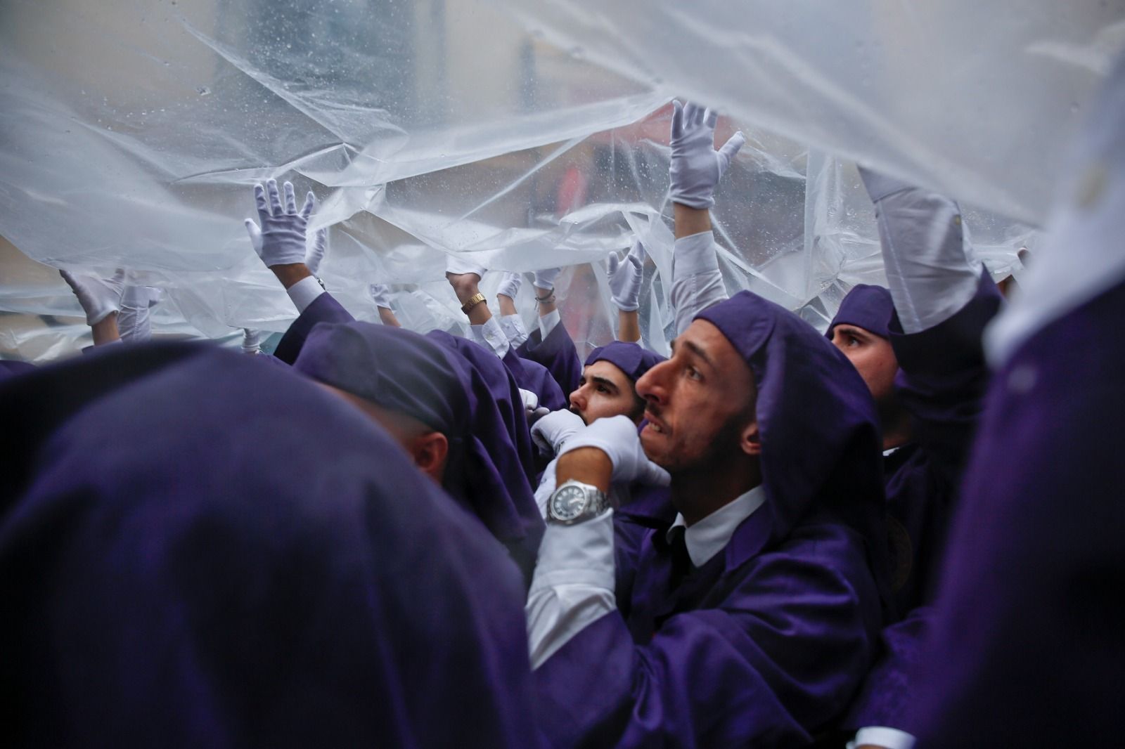 Hombres de trono protegen su imagen de la lluvia con un plástico de grandes dimensiones.