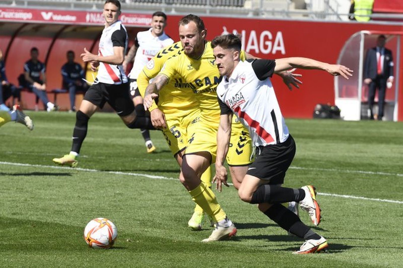 Iván Romero intenta progresar con el balón seguido por Charlie Dean.