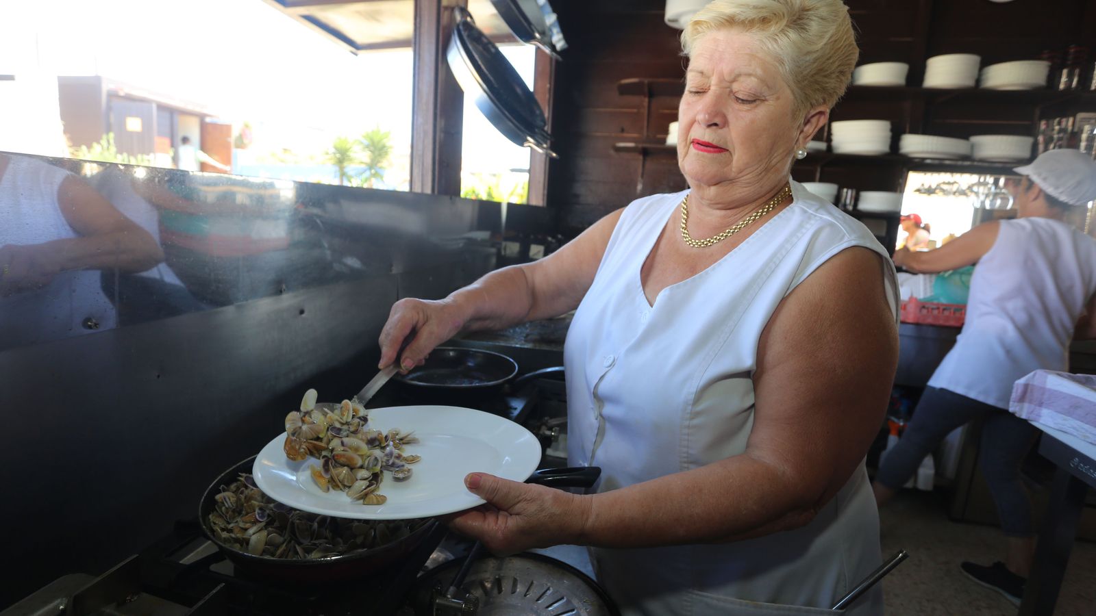 Una cocinera emplata una ración de coquinas.