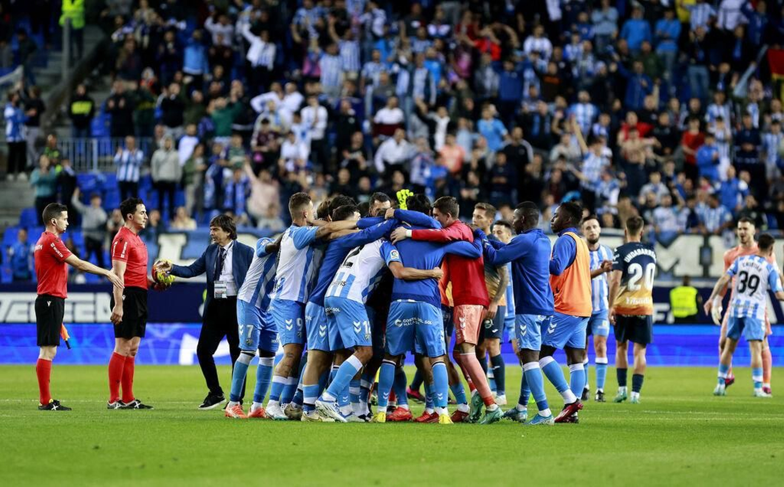 Piña de los jugadores del Málaga con la afición de fondo. Piña de los jugadores del Málaga con la afición de fondo.