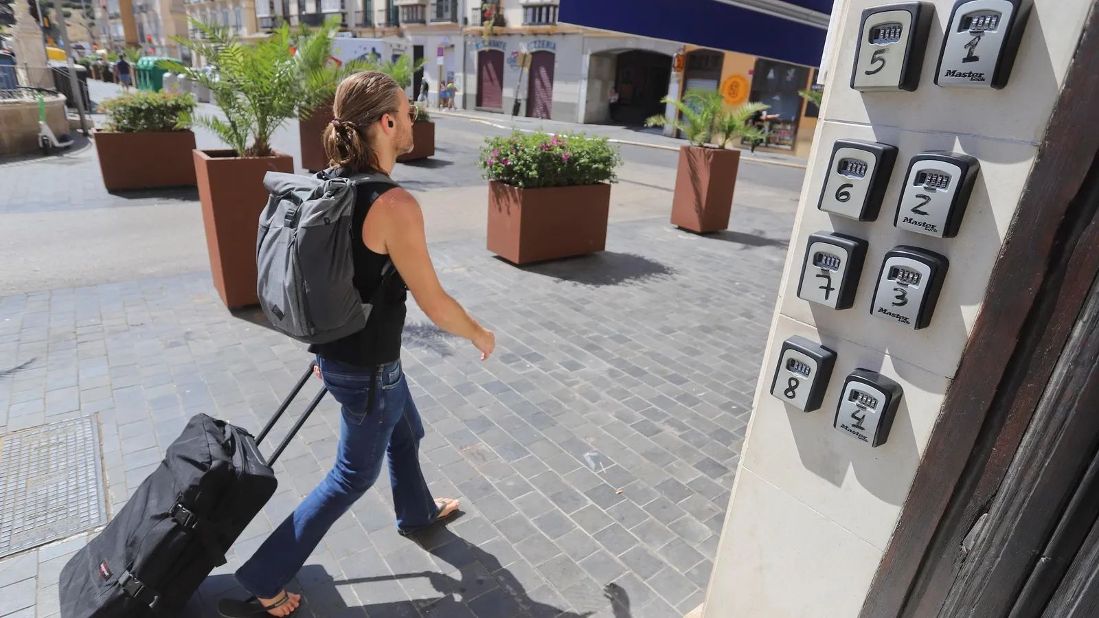 Un turista en Málaga pasao junto a un portal con cajas para llaves de pisos turísticos.