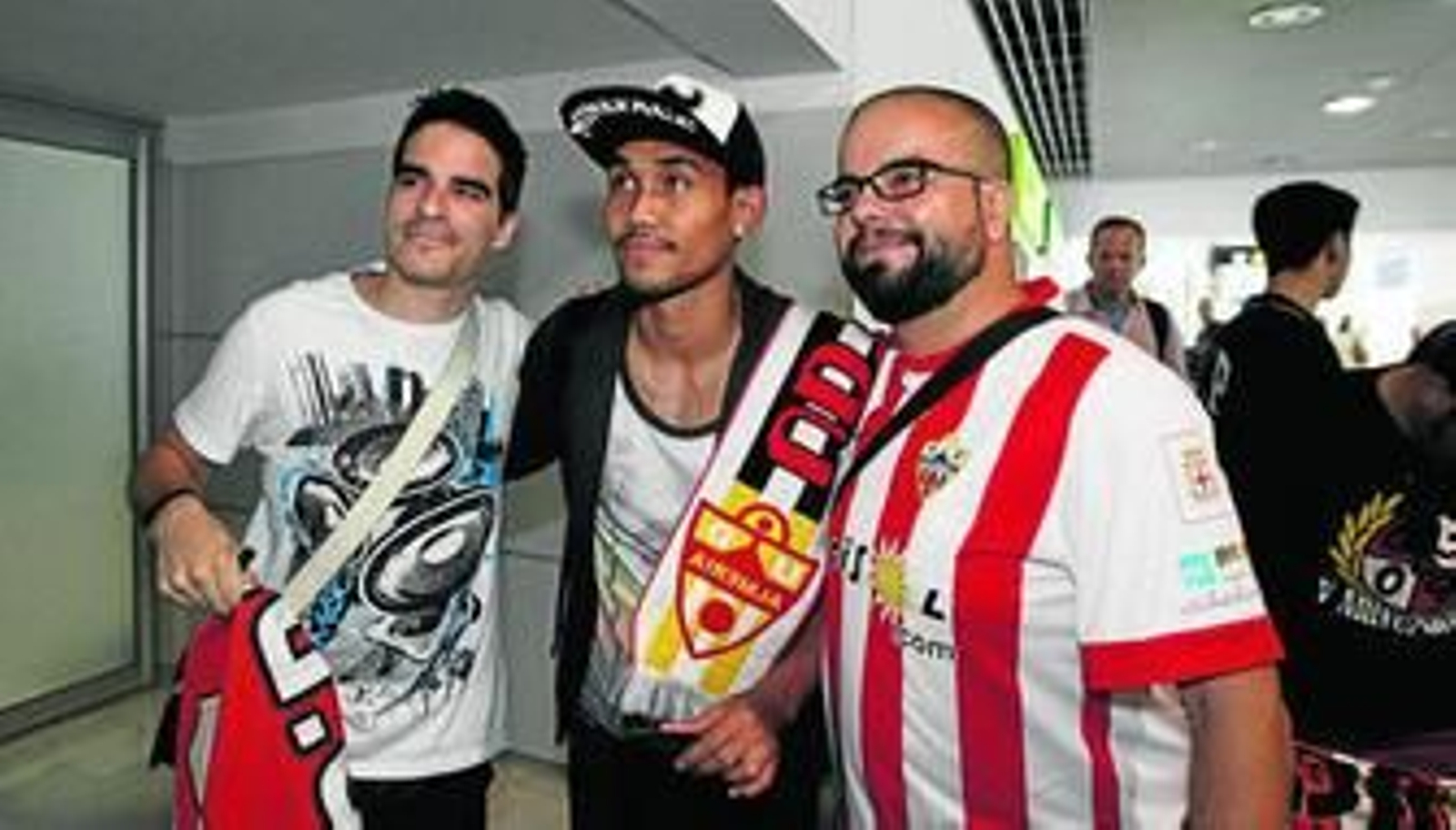 Teerasil Dangda posa a su llegada al aeropuerto con dos aficionados rojiblancos (Nacho y José Antonio) y una bufanda de la UD Almería.