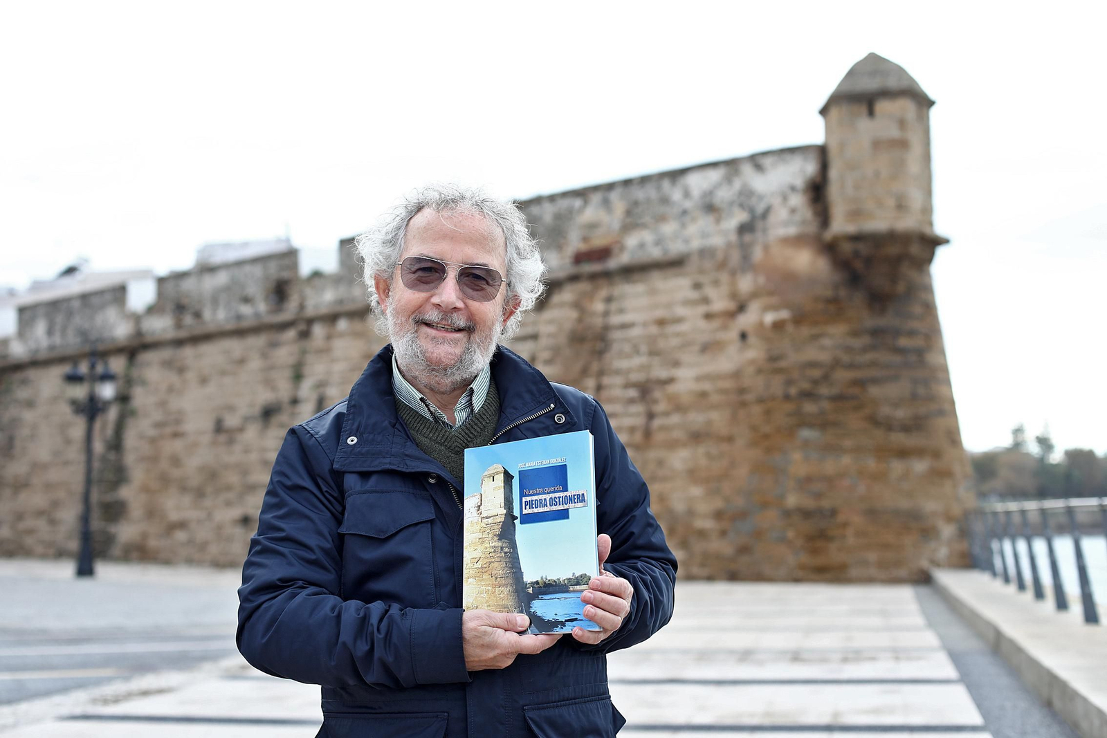 José María Esteban, con su obra, ante un tramo de la Muralla de Cádiz, levantada con piedra ostionera.