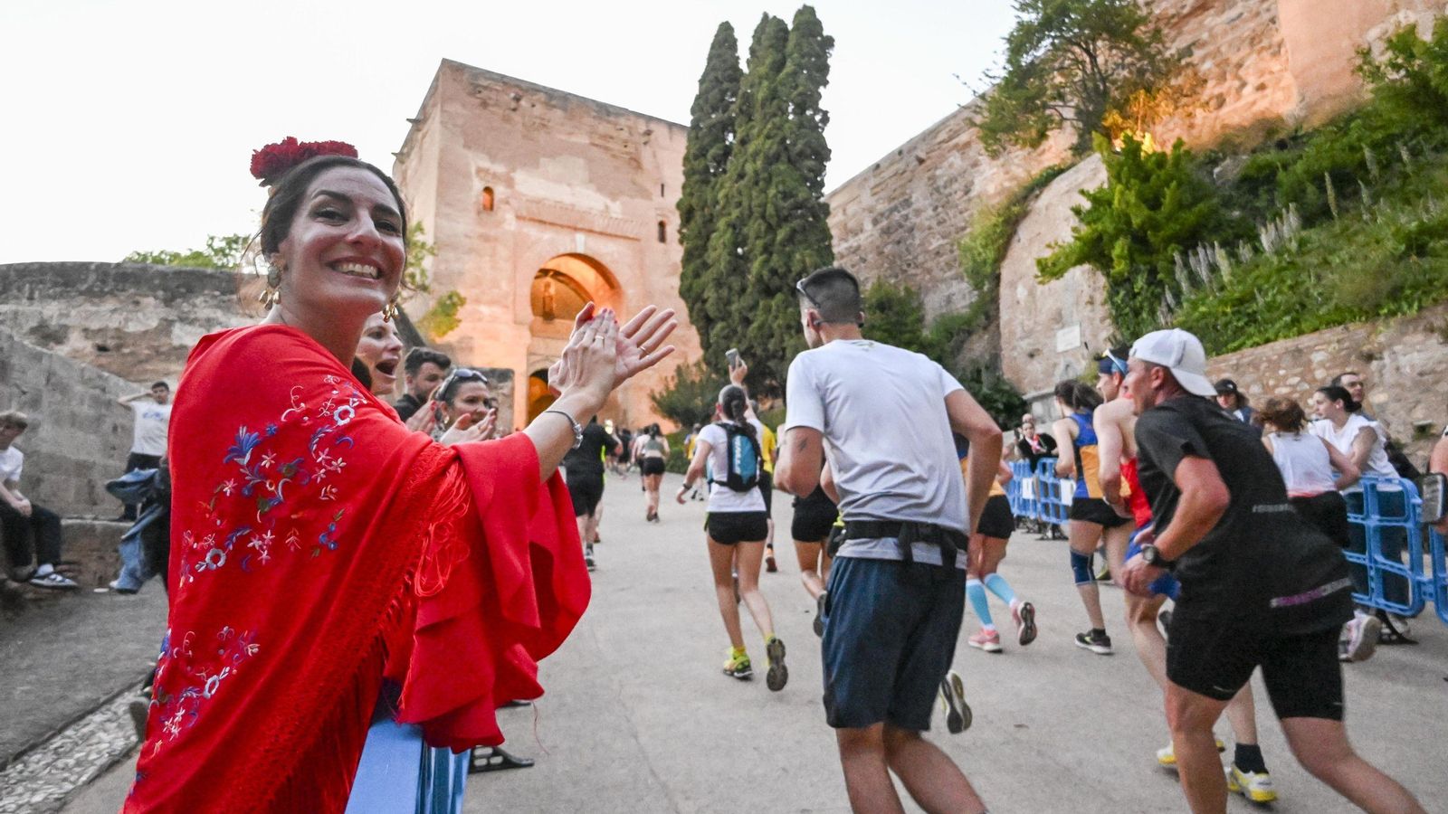 Una mujer vestida de flamenca anima a los corredores antes de la Puerta de la Justicia