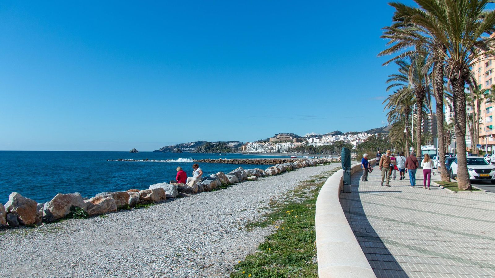 Varias personas pasean por el paseo marítimo de Almuñécar a la altura de Las Góndolas