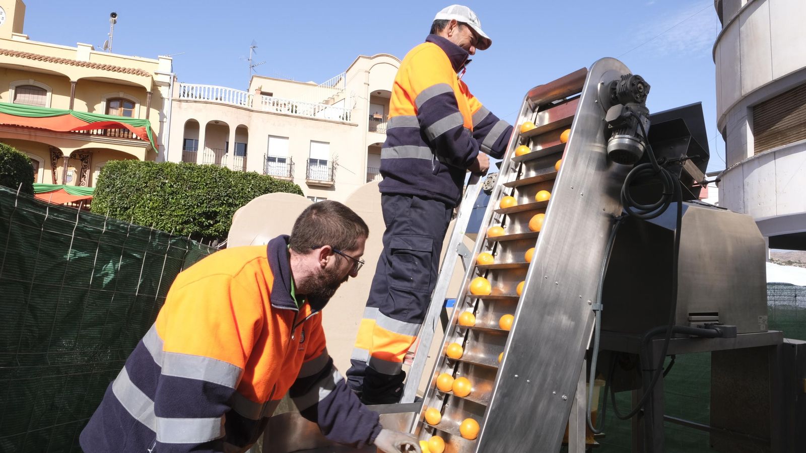 Operarios municipales abasteciendo de naranjas a la gran fuente de zumo.
