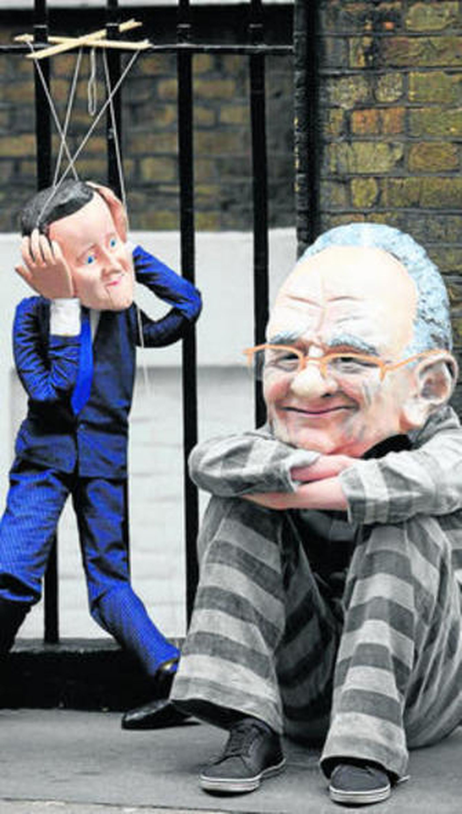 Dos personas caricaturizan a Cameron y Murdoch en Londres.