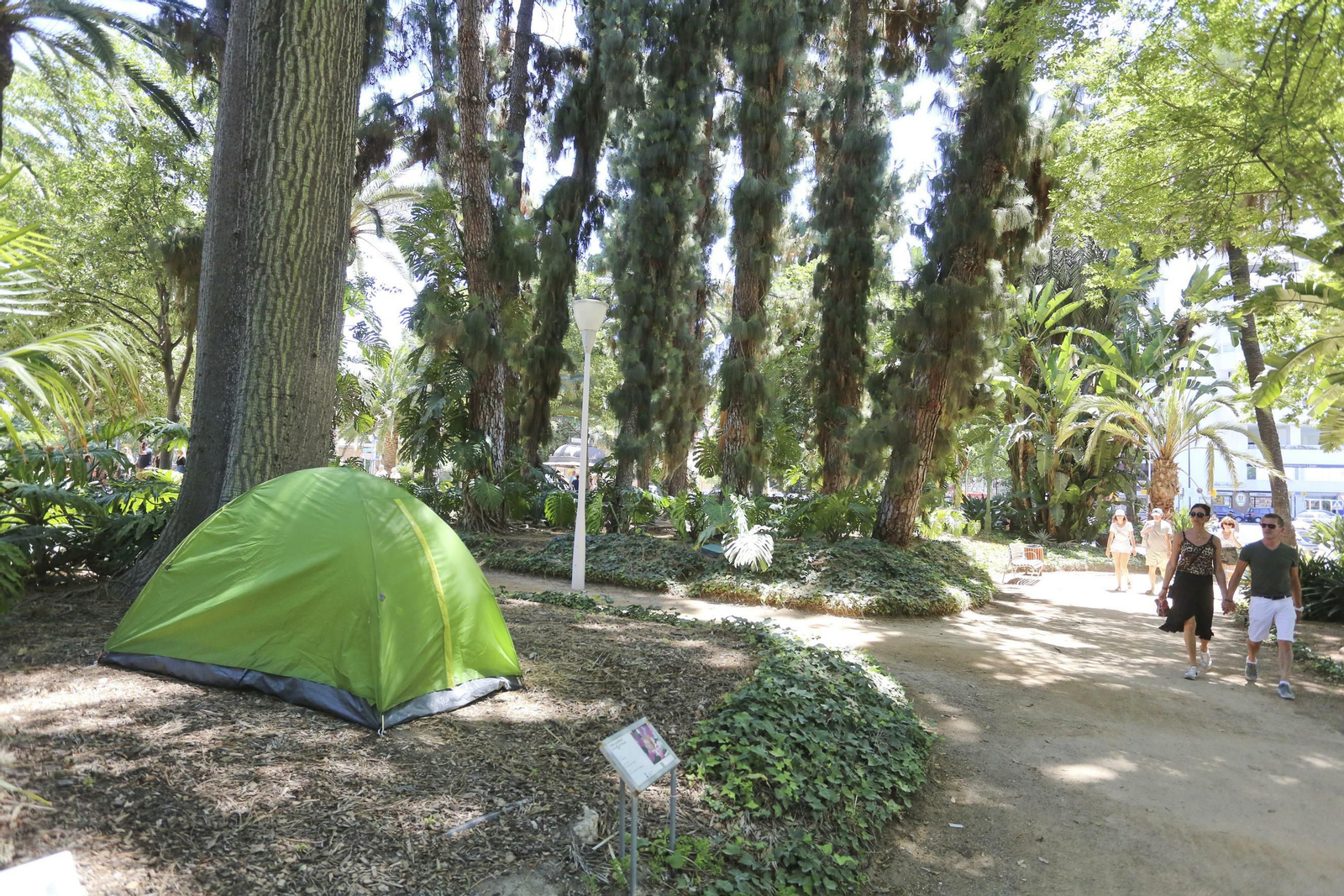 Turistas pasean junto a una tienda de campaña en el Parque de Málaga.