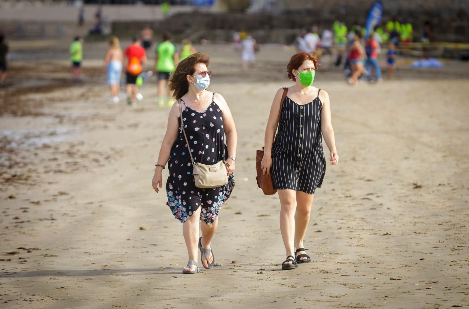 Dos personas pasean por la playa con mascarilla.