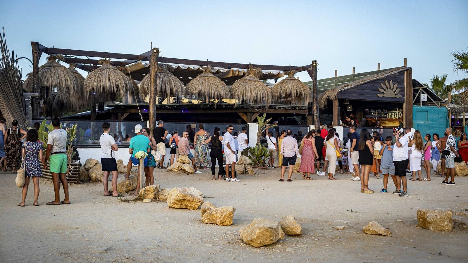 Jóvenes escuchando la música que sale de un chiringuito al atardecer.