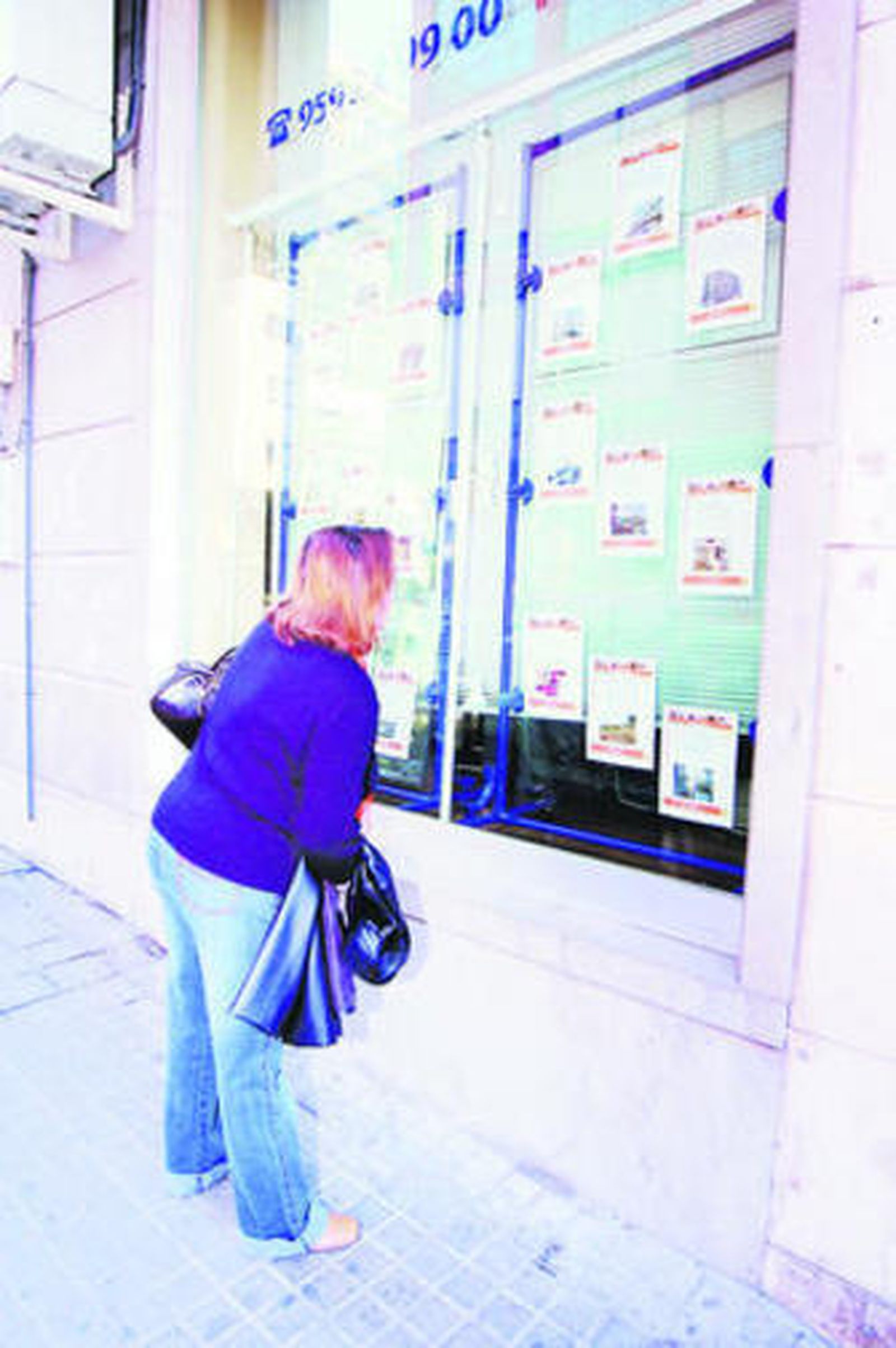 Un mujer observa el escaparate de una inmobiliaria con carteles de viviendas.