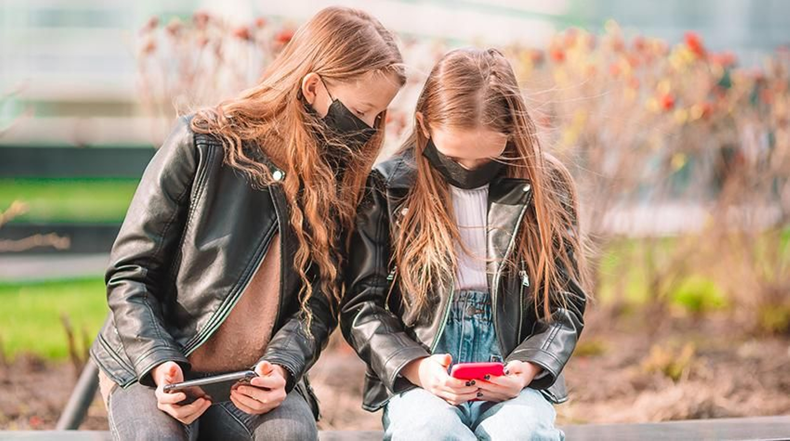 Dos menores con mascarillas y atentas al móvil.