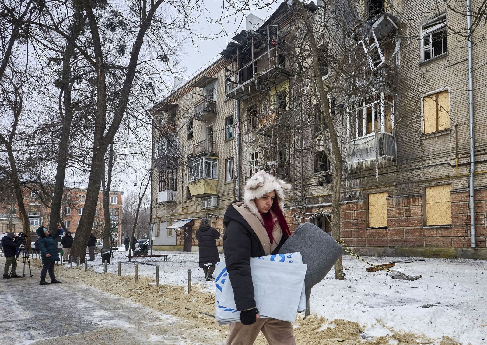 Una joven se lleva una manta distribuida por Acnur junto a un edificio residencial golpeado por los ataques rusos en Jarkov.