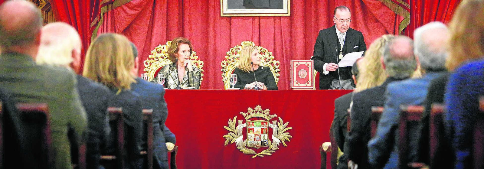 La presidenta de la Diputación, Irene García, escucha al secretario de la Real Academia, Fernando Sánchez, leyendo el acta de nombramiento de José Joly.