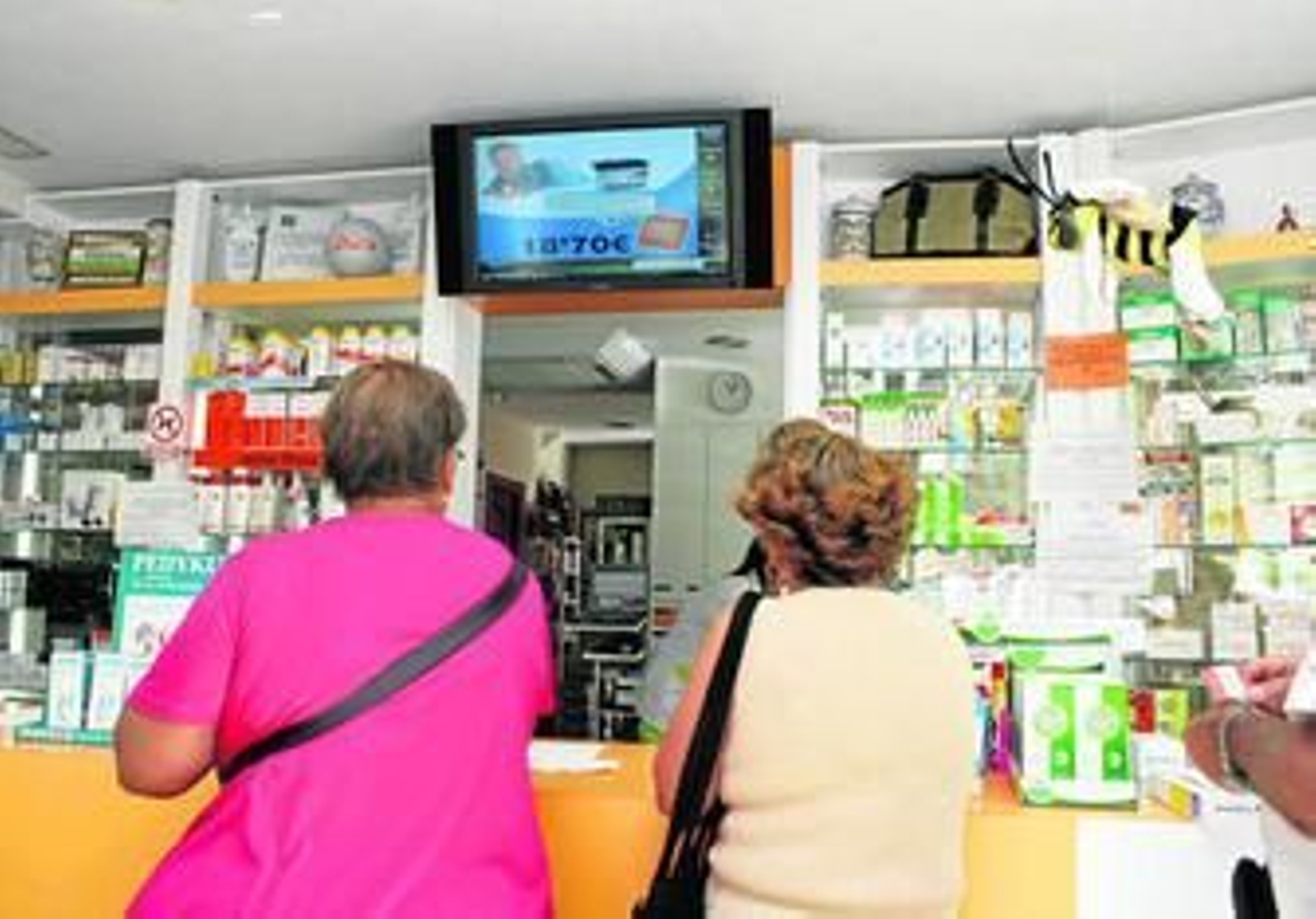 Dos usuarios aguardan en una farmacia a ser atendidos.