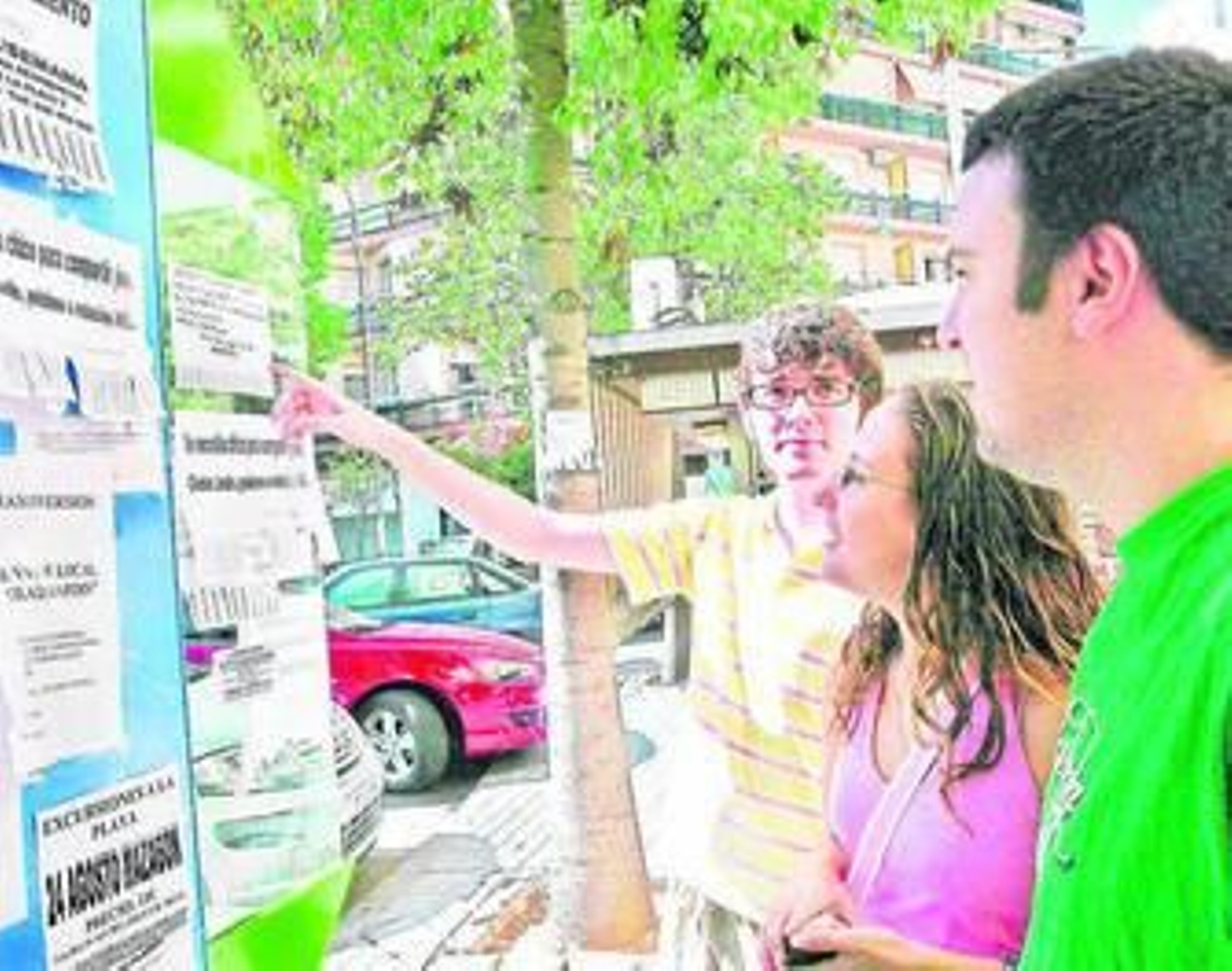 Varios jóvenes observan los anuncios de pisos pegados en una cabina de teléfono.