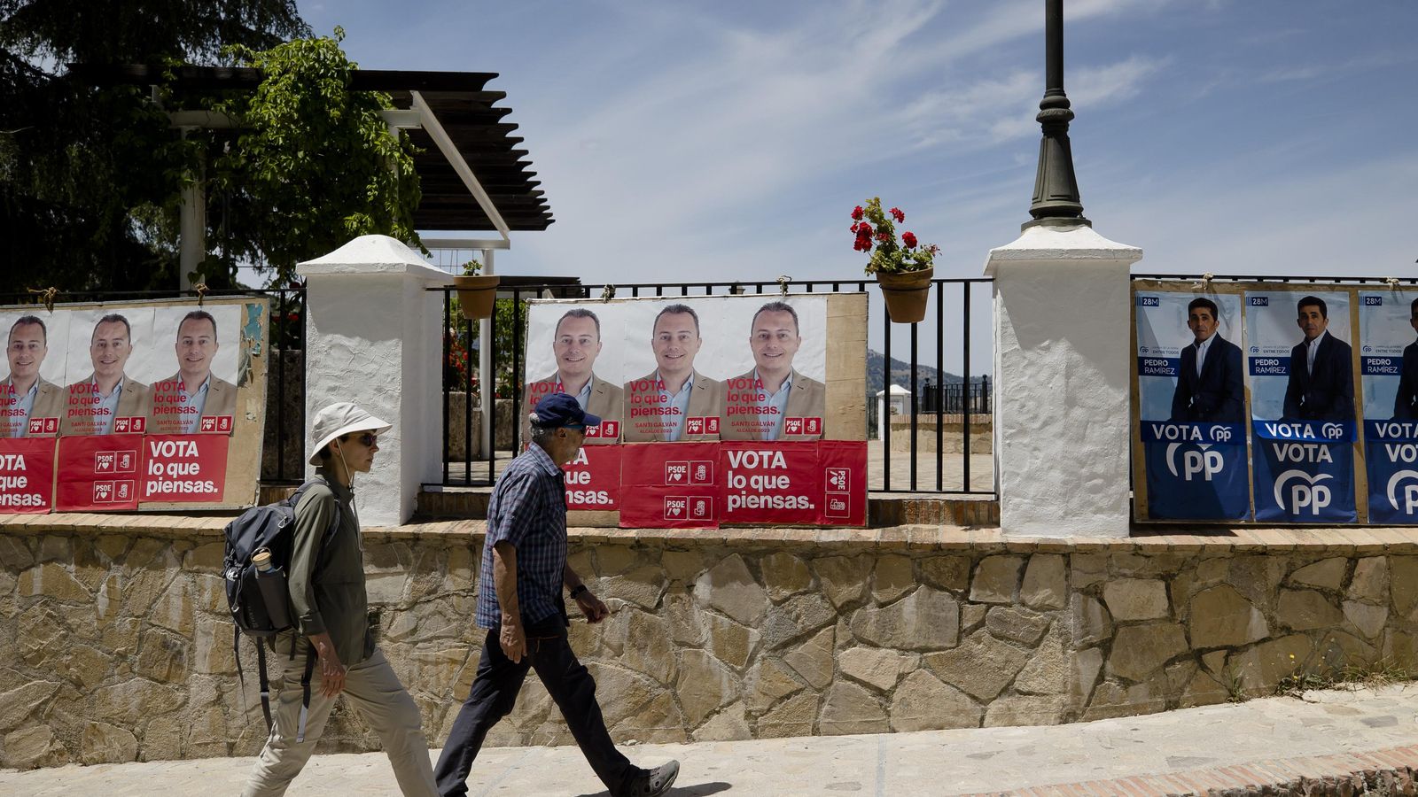 Turistas pasean frente a los carteles electorales de los candidatos de los dos principales partidos.