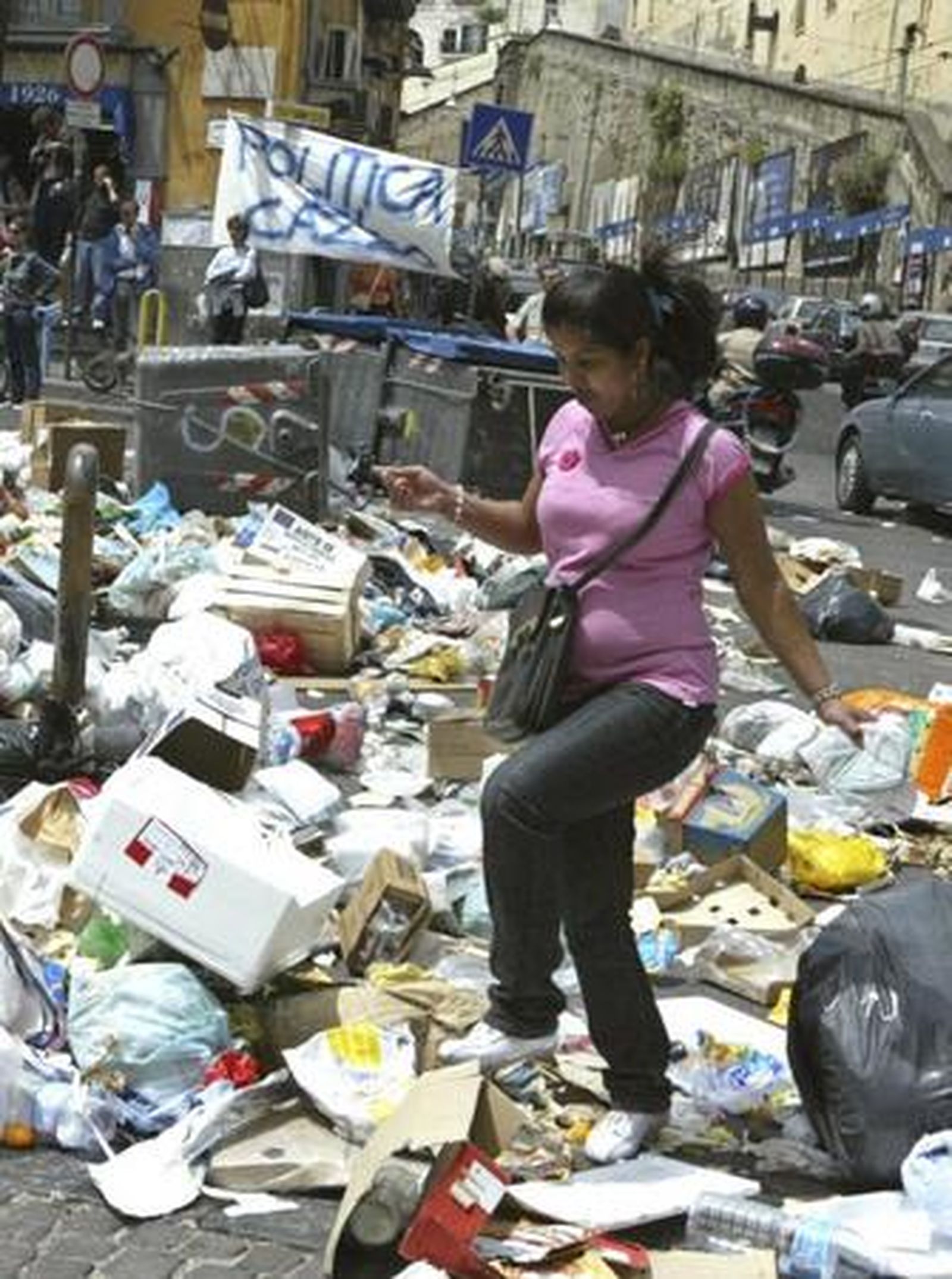 Una mujer cruza una calle entre montones de basura.