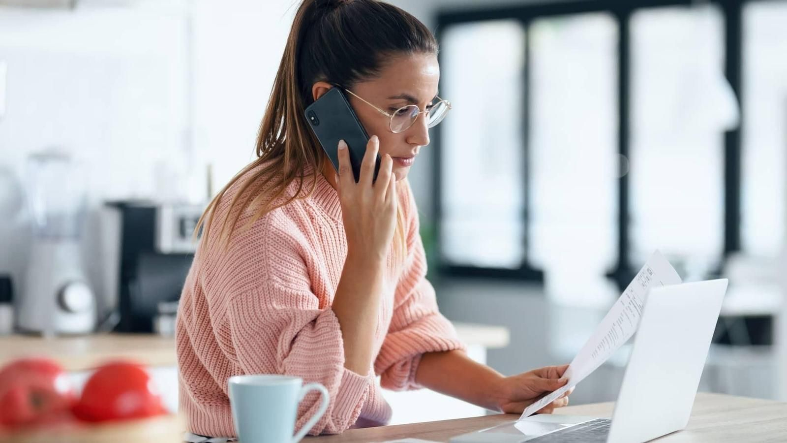 Una mujer habla por teléfono mientras consulta su ordenador
