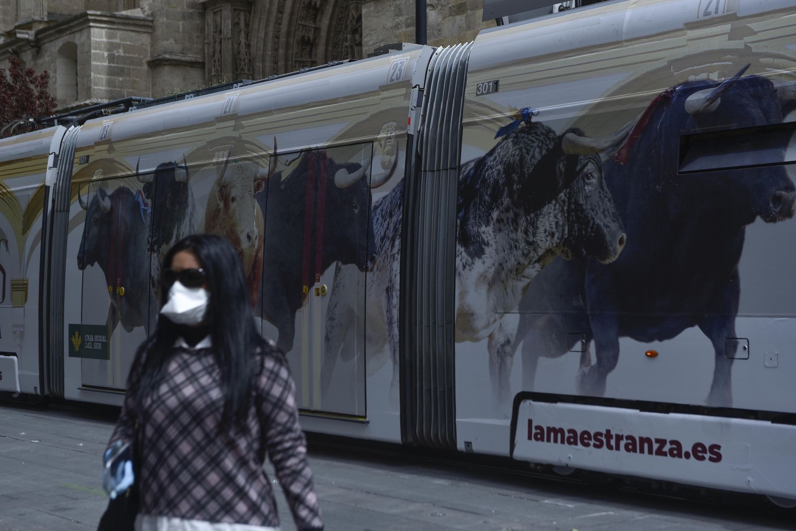 Una mujer con mascarilla camina junto al Metrocentro, decorado con un anuncio sobre los toros.
