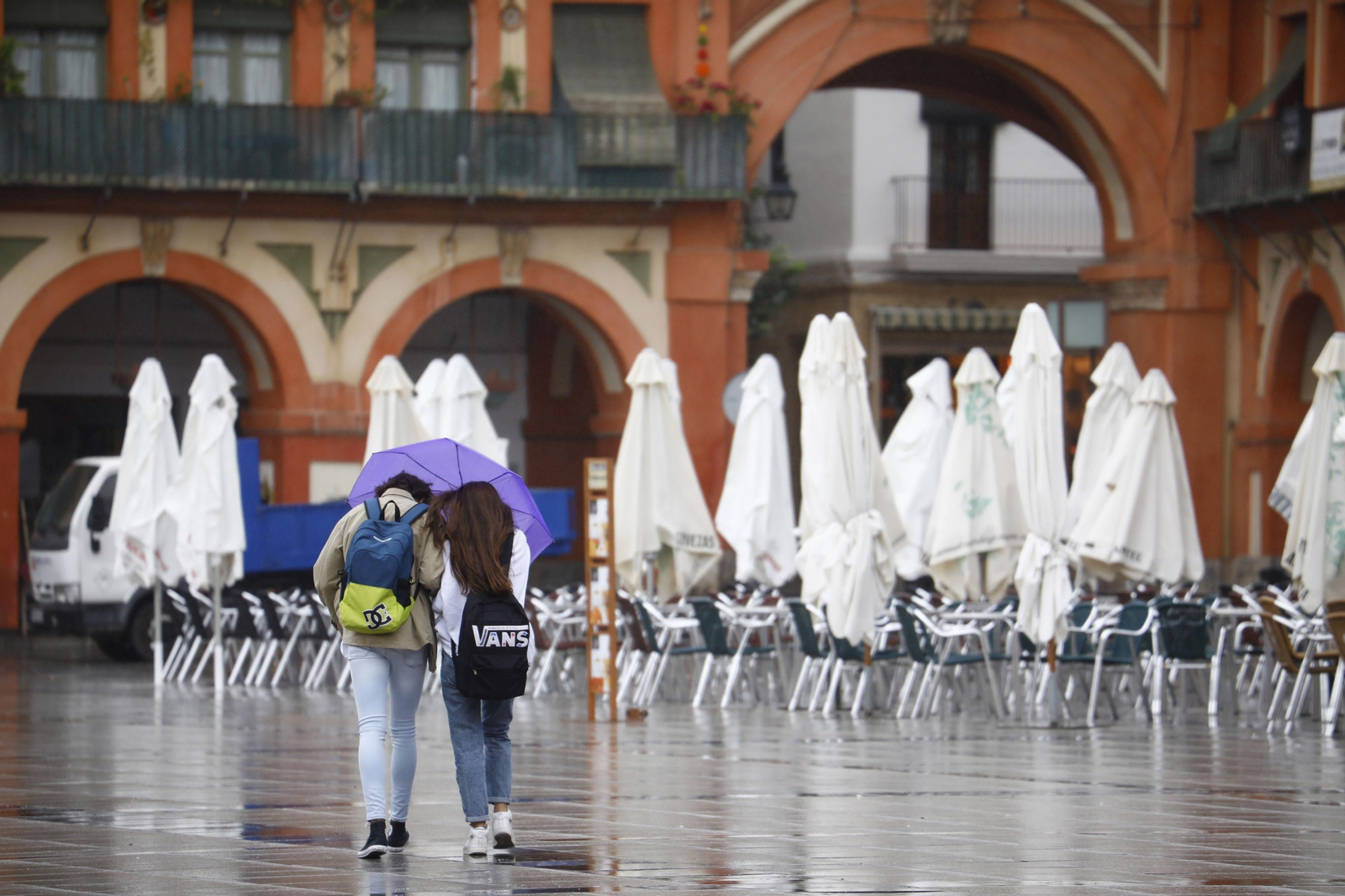 Dos personas caminan bajo la lluvia por la plaza de la Corredera.