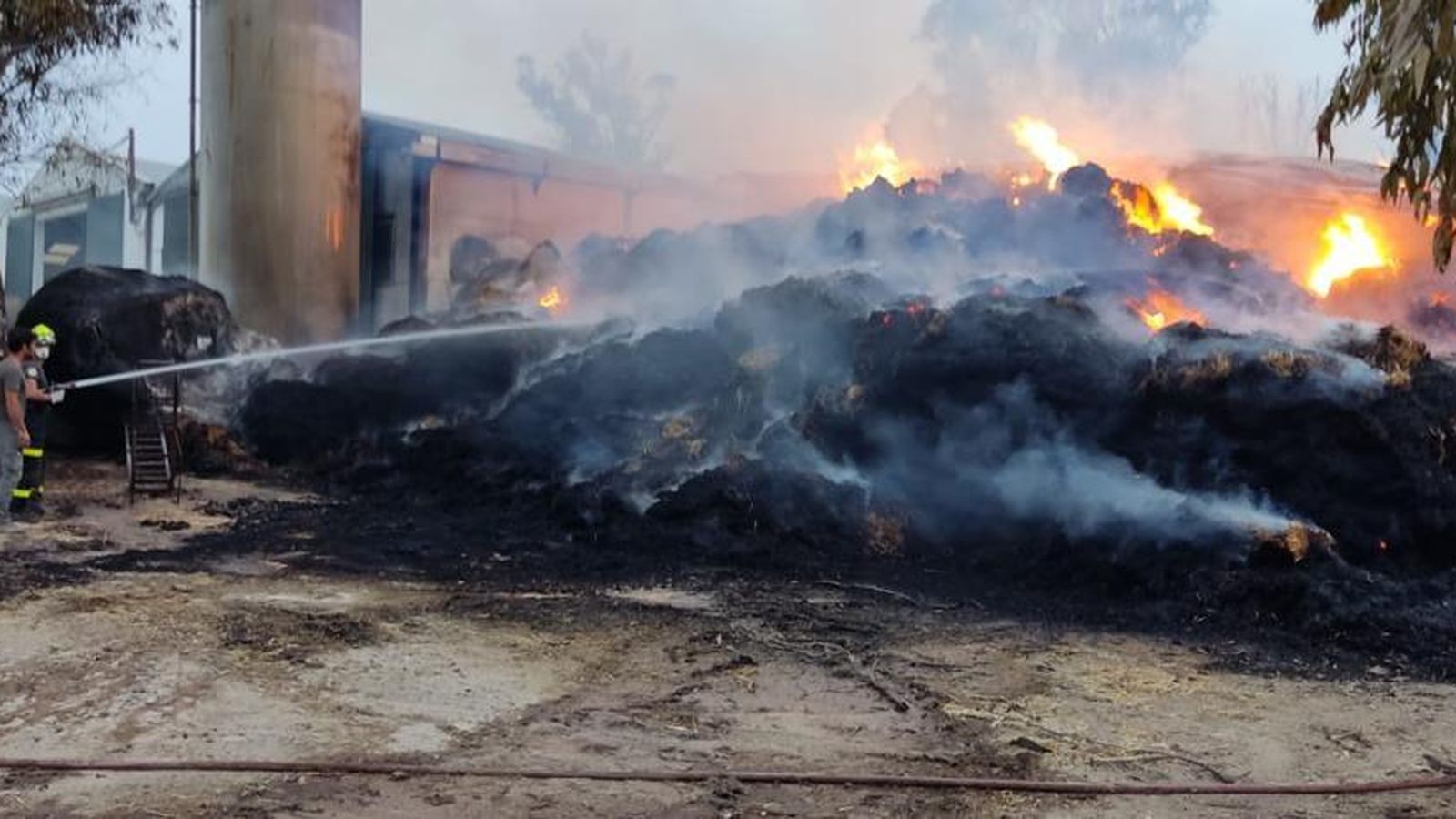 Un bombero sofocando la inmensa montaña de balas de paja quemadas por el fuego