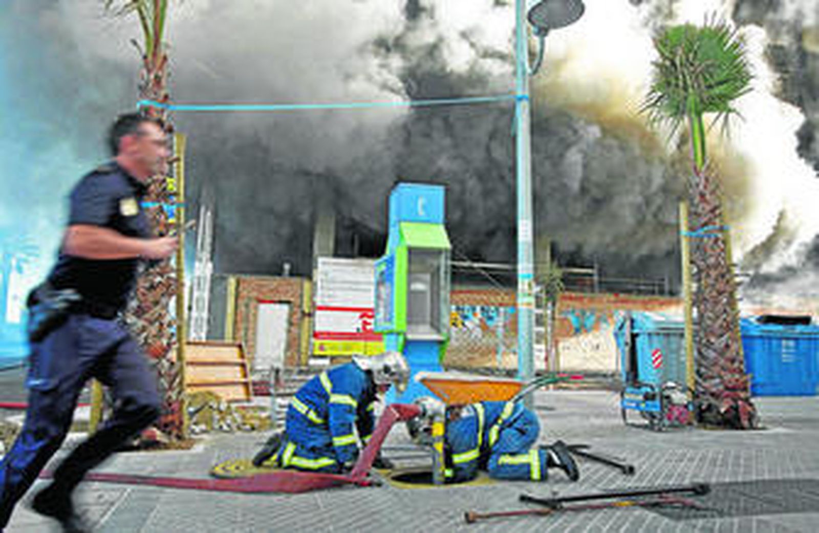 Un policía corre a atender a los afectados, mientras dos bomberos conectan una manguera a la red.