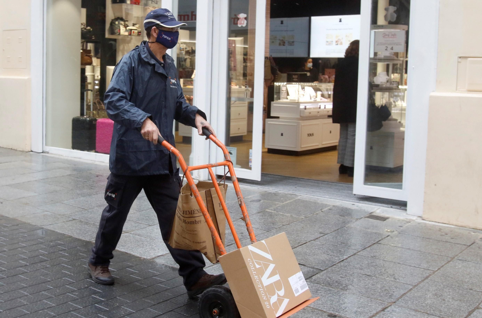 Un repartidor lleva unos paquetes en una carretilla.