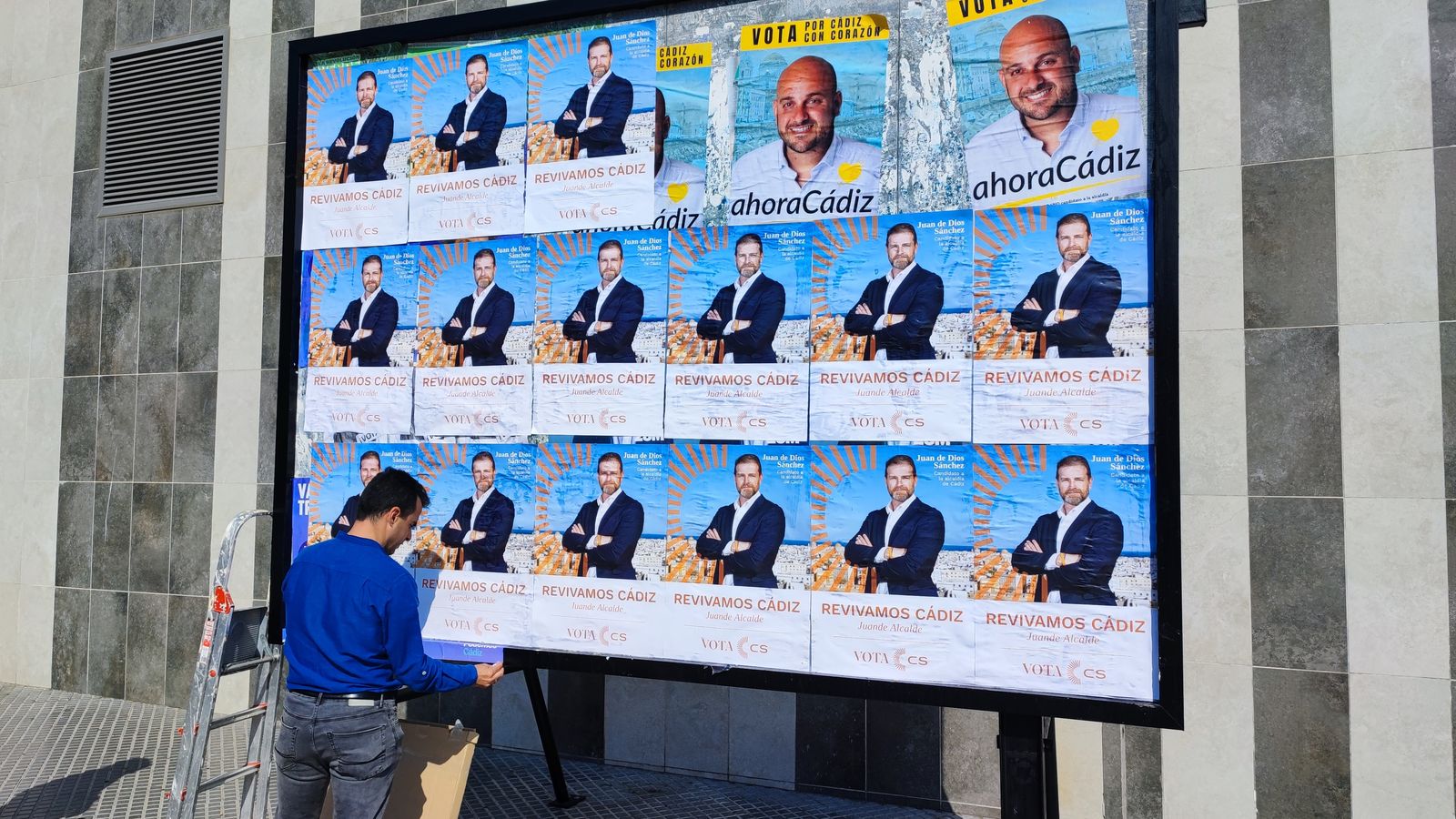 Un trabajador o voluntario de Cs repone los carteles de Juan de Dios Sánchez.
