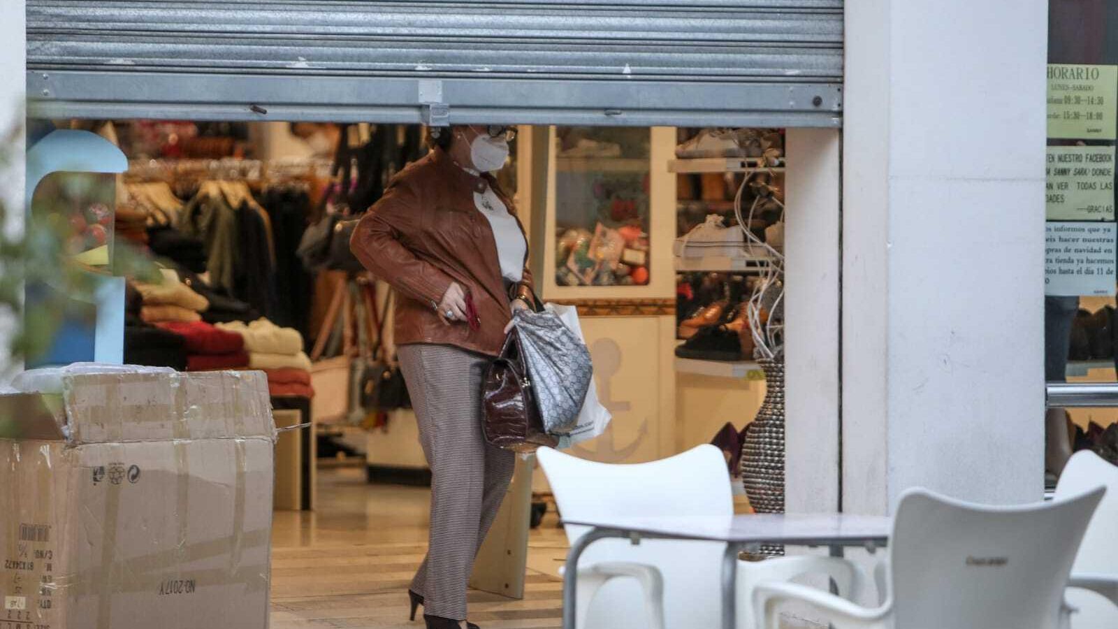 Una clienta sale de una tienda minutos antes de las seis de la tarde con la reja a medio bajar.