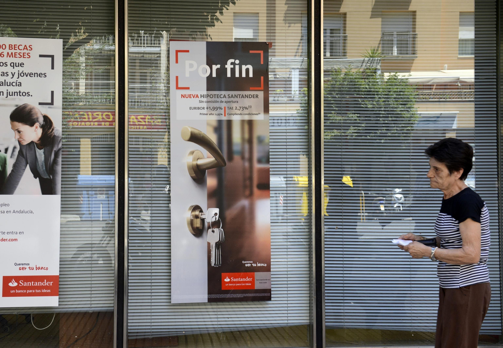 Una mujer pasa frente a una sucursal bancaria con un anuncio de hipotecas