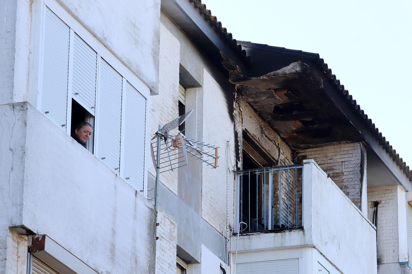 Una vecina se asoma a una ventana junto a la vivienda incendiada esta mañana.