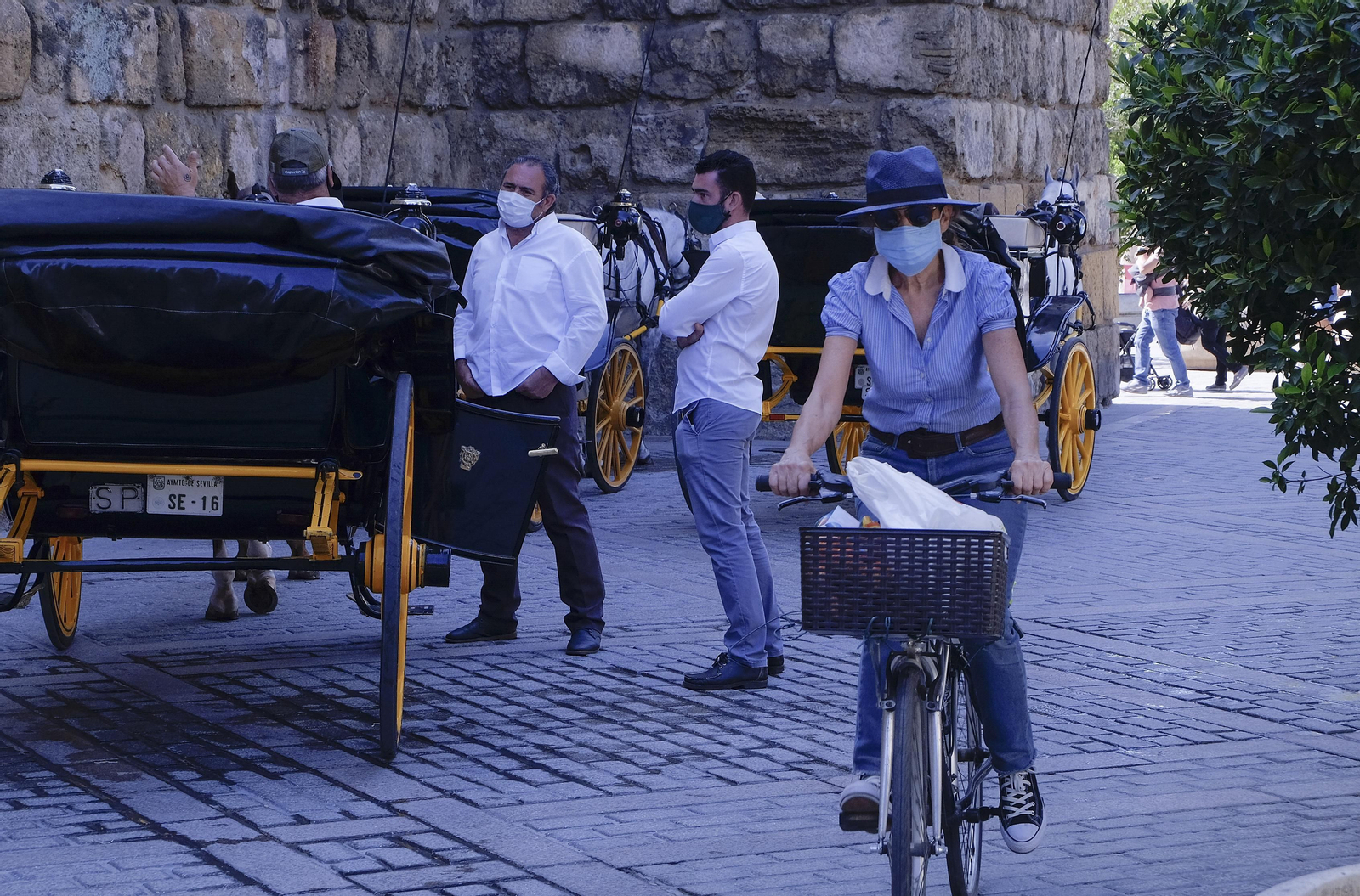 Una mujer pasea en bici junto a una parada de coches de caballos.